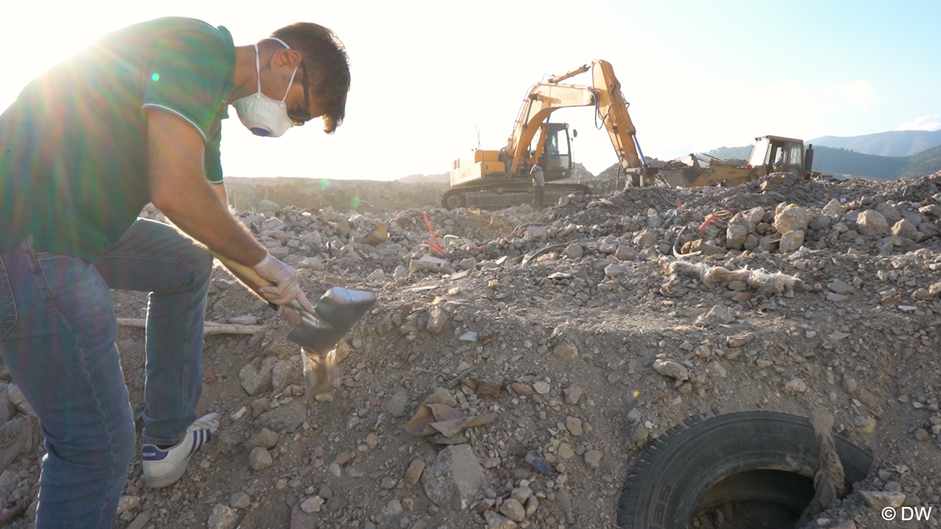 Utku Firat wears a mask as he uses a small shovel to fill dust into a small plastic bag on a debris site in Hatay, southern Turkey (image: DW)