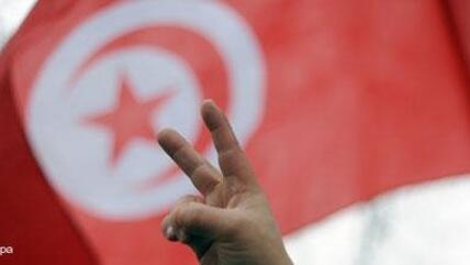 Demonstrant zeigt vor tunesischer Nationalfahne das Victory-Zeichen; Foto: dpa