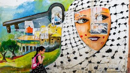 تلميذة فلسطينية تمر بجانب رسمة جدارية معبرة عن النكبة في مخيم جنين للاجئين.