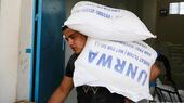 A man carries two UNRWA sacks of wheat flower on his shoulder as he walks through a blue door