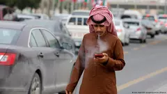 رجل سعودي يدخن سيجارة ويقرأ شيئا على هاتفه المحمول في الرياض.