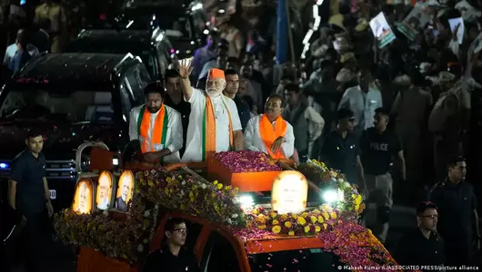 Indian Prime Minister Narendra Modi, wearing a saffron cap, greets supporters from an open vehicle