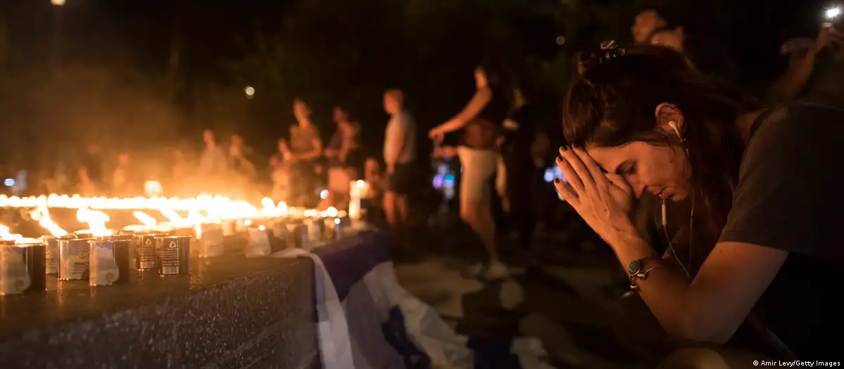 People kneel in grief in front of a sea of lit candles