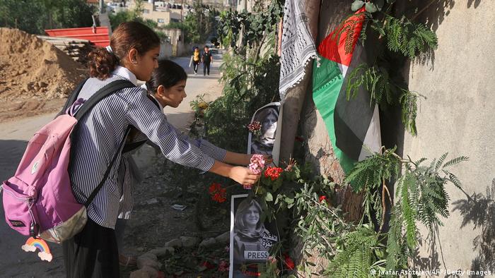 Zwei Mädchen legen Blumen ab, die Todesstelle ist mit Fotos der Getöteten sowie Palästinensertuch und -flagge geschmückt