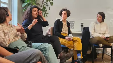 Five people (including, from left, Tom Kellner, Seba Abu Daqa, Gali Blay and Elisha Baskin) sit on chairs in a room; one is talking, all others are looking at her